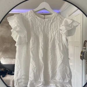 Vit blus med volangärm från Name It - Supersöt vit blus från Name It med volangärmar och broderade små prickar. Väldigt stor i storleken så passar mig som är 172cm lång. Den har lite missfärgning under armarna och i nacken men inget som syns tydligt. 💕