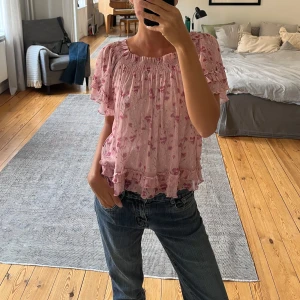 Blommig blus - Supersöt blommig blus i ljusrosa från Pull&Bear. Modellen har korta volangärmar, smockad halsringning och volangdetaljer längst ner. Tunt och luftigt material. Går även att bära som offshoulder. 