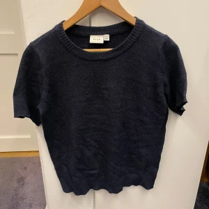 Mörkblå stickad tröja från Vila - En enkel och snygg mörkblå stickad tröja från Vila i storlek S. Tröjan har rund halsringning, korta ärmar (avklippta hemma) och ribbade muddar vid hals och nederkant. Perfekt för dig som gillar stilrena och bekväma plagg med lite loose passform. diskuterar gärna pris