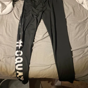 Svarta leggings med tryck #SQUAD - Svarta leggings med vitt tryck #SQUAD längs ena benet. Tight passform och stretchigt material som passar perfekt till träning eller chill. Snygga att matcha med oversized hoodie eller crop top. Rekommenderas för barn runt 12-13 år