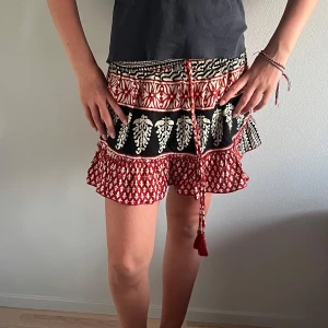 Röd mönstrad kort kjol med volang - Kort kjol i rött, svart och vitt mönster med volang och snörning i midjan. Lätt bomullstyg med unika detaljer. KuiNi, storlek S, nytt skick. Nypris 500 kr – säljes för 250 kr! ❤️❤️