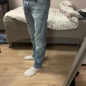 Ljusblå jeansbyxor i rak modell - Säljer ett par ljusblå jeansbyxor i rak passform med klassisk femficksdesign. Jeansen har normal midja och är tillverkade i bomullstyg med snygga slitningar och kontrastsömmar. Perfekta för en avslappnad och stilren look.