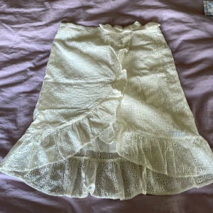 Vit volangkjol från WE - Supersöt vit kjol från WE med broderade hålmönster och bred volangkant längst ner. Kjolen har omlott-design framtill och resår i midjan för skön passform. Perfekt för dig som gillar romantisk och feminin stil.