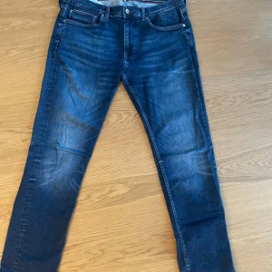 Mörkblå jeans från Tommy Hilfiger - Snygga mörkblå jeans från Tommy Hilfiger med klassisk femficksdesign och diskret logga på bakfickan. Jeansen har raka ben och en normal passform, tillverkade i mjukt bomullstyg med lite stretch.