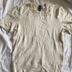 Beige stickad kortärmad tröja H&M - Enkel och stilren beige stickad tröja från H&M Divided. Kortärmad modell med rund halsringning och ribbade kanter. Perfekt för lager-på-lager eller sommarens chill outfits. Mjuk och skön känsla i materialet. Hel och ren men lite nopprig.