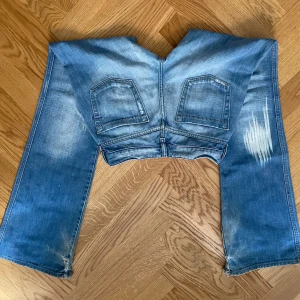 Blå bootcut jeans med slitningar - Supersnygga diesel jeans med bootcut passform och slitna detaljer på benen. Längst ner vid fötterna är de slitna vilket syns på sista bilden.