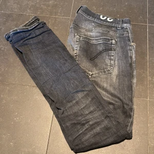 Dondup George - Säljer ett par mörkgrå jeans med snygga slitningar och ljusa tvättade partier. Jeansen har klassisk femficksdesign, smal passform och knäppning fram. Perfekta för dig som gillar en avslappnad men trendig look. Dom är modellen ”George”
