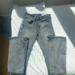 Grå bootcut jeans från Vero Moda - Snygga grå jeans från Vero Moda med bootcut-ben och hög midja. Jeansen har klassisk femficksdesign, bälteshällor och är tillverkade i stretchig denim för en bekväm passform. Perfekta för dig som gillar en trendig och avslappnad look.