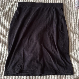 Svart kortkjol från 157 i bomull - Enkel svart kortkjol från 157 i mjuk bomull. Kjolen har rak passform och resår i midjan för en bekväm känsla. Perfekt att matcha med en crop top eller hoodie för en chill look. Kjolen ser lite röd ut i bilden med den är inte det.