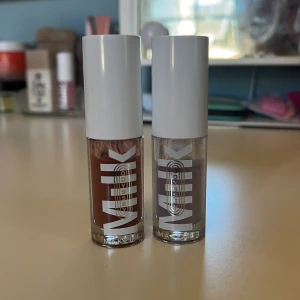 Milk Makeup läppglans duo - Två läppglans från Milk Makeup med vita lock och genomskinliga hylsor. Ena är brun med krämig finish, den andra är ljuslila med skimrande effekt. Båda har mjuka applikatorer som gör det enkelt att få ett jämnt resultat. Perfekt för dig som gillar att variera din look.