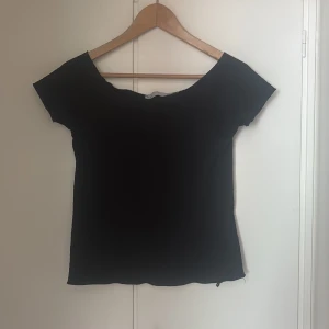 Svart ribbad topp med kort ärm - En svart, ribbad topp med korta ärmar och rundad halsringning. Tyget är stretchigt. Passformen är normal och toppen är lätt croppad i modellen. Storlek M