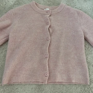 Ljusrosa stickad kofta från Gina Tricot - Supermysig ljusrosa stickad kofta från Gina Tricot i storlek 158/164. Koftan har rund hals, långa ärmar och knäpps med fem matchande knappar framtill. Perfekt att slänga på sig när det är lite kyligt ute. Ribbad struktur och mjukt material.