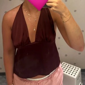 Vinröd halterneck linnetopp - Säljer en vinröd halterneck linnetopp med djup v-ringning och knyt i nacken och ryggen. Toppen är ärmlös och har en slät, lätt glansig yta som ger en snygg look. Perfekt för dig som vill sticka ut med en enkel men trendig topp💕