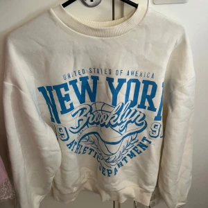 Vit sweatshirt med blå New York-tryck - Säljer en vit sweatshirt med stort blått New York Brooklyn-tryck på framsidan. 