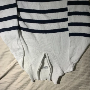 Vit och marinblå randig stickad tröja - Säljer en vit stickad tröja från Lindex med marinblå horisontella ränder. Tröjan har långärmade ribbade muddar och en half zip-dragkedja framtill. Materialet är mjuk bomull och passformen är normal. Perfekt för dig som gillar klassisk och chill stil.