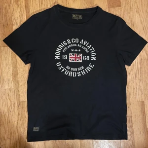 Svart t-shirt från Morris - Svart t-shirt från Morris med tryck på Union Jack och texten 'Morris & Co Aviation Oxfordshire' på bröstet. Klassisk rund hals och korta ärmar. Skön bomullskvalitet och normal passform. Perfekt för dig som gillar brittisk vintage vibe.                                Kom gärna med prisförslag!