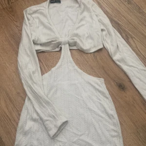 Vit omlottklänning från SHEIN - Säljer en vit kortklänning från SHEIN med långärmad design och snygg omlott-detalj framtill. Klänningen har öppen rygg och ett coolt cut-out parti under bysten. Materialet är mjukt och har ett diskret mönster som ger extra stilpoäng.