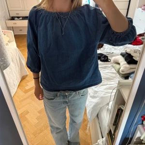 Jeanstopp - Säljer en snygg blå blus/topp i jeansliknande tyg. Går att bära både off shoulder, snett över axeln och vanlig rund halsad. Blusen har en loose passform och trekvartsärmar.