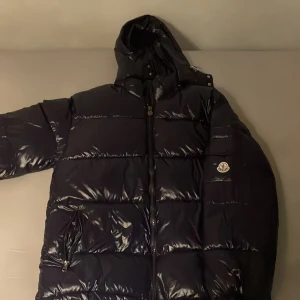 Mörk blå Moncler pufferjacka med huva - PRIS KAN DISKUTERAS .Säljer en mörkblå, glansig pufferjacka från Moncler med huva och dragkedja framtill. Jackan har Moncler-logga på ärmen och stora, quiltade sektioner. Perfekt för kalla dagar och riktigt snygg streetstil. 
