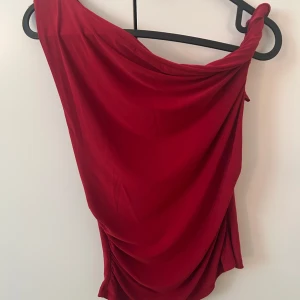 Röd oneshoulder top Pull&Bear - Säljer en snygg röd kortklänning från Pull&Bear i oneshoulder-modell. har draperad design och är tillverkad i mjukt, slätt material som ger en cool och modern look. Perfekt för dig som vill sticka ut med en färgstark och trendig stil.