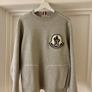 Grå sweatshirt Moncler - Storleken är XL men som Moncler är så sitter den som L/M. Säljer en stilren grå sweatshirt från Moncler med ett stort broderat märke på bröstet. Med fickor på vars en sida. 