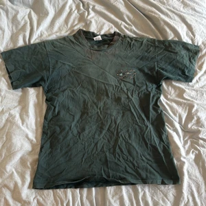 Vintage L T-shirt från Quiksilver - Säljer en grön t-shirt från Quiksilver med ett stort tryck på baksidan. T-shirten har korta ärmar och en rund halsringning. Perfekt för en avslappnad stil.
