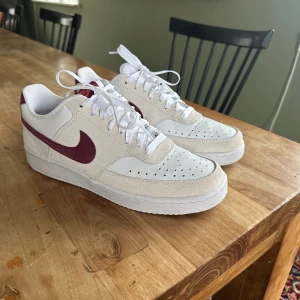 Nike sneakers i vitt och vinrött - Snygga Nike sneakers i vitt och beige med vinröda detaljer. Väldigt fint skick, sparsamt använda. Storlek 41.