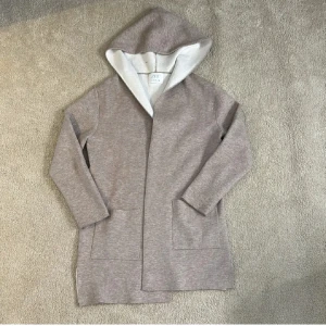 Beige långärmad kofta från Zara - Mysig beige långärmad kofta från Zara med en skön huva och praktiska fickor framtill. Perfekt för kyliga dagar och enkel att matcha med andra plagg. Lite nopprig i armarna men annars är den i bra skick💕