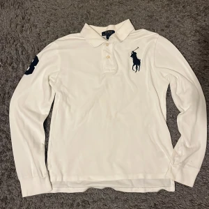Vit långärmad pikétröja från Ralph Lauren - STORLEK L 14-16 år, INTE L I HERR STORLEK klassisk vit pikétröja från Ralph Lauren med loggan broderad i mörkblått på bröstet. Två knappar vid bröstkorgen som går att knäppa. Otroligt snygg och klassisk. Har använts förr och har älskat denna men den har blivit för liten för mig nu. Perfekt för kommande sommaren!!