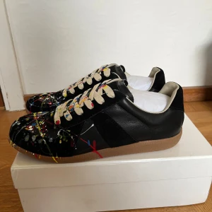 Maison Margiela  - Unika svarta sneakers från Maison Margiela i storlek 43. Skicket är 10/10. Skorna har en klassisk design. Perfekta för dig som vill sticka ut med en konstnärlig touch.