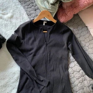 Svart ribbad tröja med dragkedja - Snygg svart ribbad tröja med dragkedja framtill. Tröjan har långa ärmar och en stilren design som passar perfekt till olika outfits. Perfekt för en cool och avslappnad look.