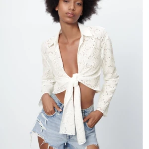 Vit blus med knytning - Snygg vit spetsblus med knytning framtill. Blusen har långa ärmar och en croppad passform som ger en trendig look. Perfekt för varmare dagar eller sommarens fester.
