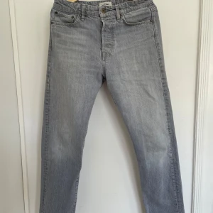 Grå jeans från Jack & Jones - Snygga grå jeans från Jack & Jones med klassisk femficksdesign. De har en rak passform och är tillverkade i ett slitstarkt denimtyg. Perfekta för en avslappnad stil.