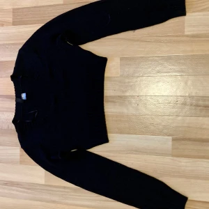 Svart stickad tröja från H&M  - Säljer en svart stickad tröja från H&M. Tröjan är croppad med långa ärmar och har en ribbad kant vid halsen och ärmkanten. 💕💕💕