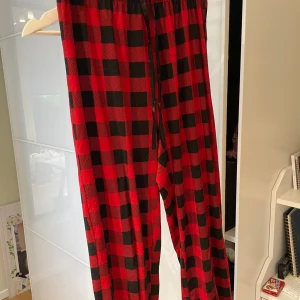 Röda och svarta rutiga byxor - Snygga och bekväma byxor i röd och svart rutig design. De har en elastisk midja med snörning för justerbar passform. Perfekta för en avslappnad stil. 