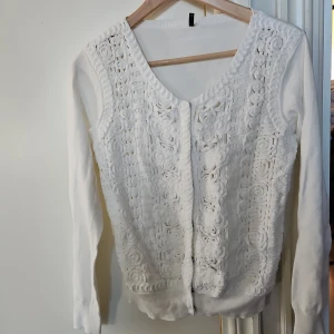 Vit kofta nyskick  - Vit kofta med långa ärmar och ett dekorativt, blommigt mönster på framsidan. Koftan har en v-ringning och knäpps med knappar.
