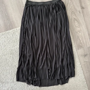 Svart plisserad kjol - Snygg svart plisserad kjol med elastisk midja. Kjolen har en elegant och flytande design som passar perfekt för olika tillfällen. Den är gjord i ett lätt och bekvämt material som ger en fin rörelse. Från gekås