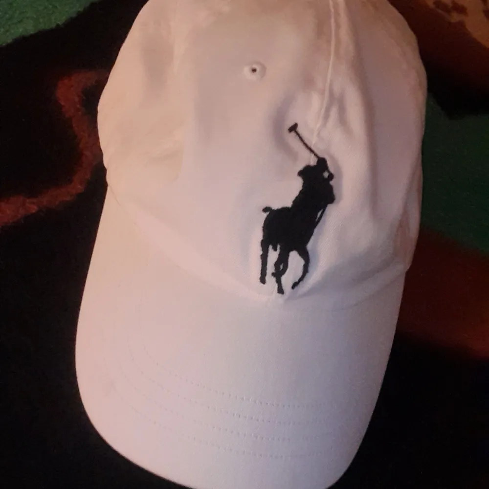 Snygg vit keps från Polo Ralph Lauren med den ikoniska broderade polospelaren i svart framtill. Kepsen har även en broderad siffra '3' på sidan och texten 'POLO' baktill. Justerbar passform med bälte baktill för optimal komfort.ordinarie pris 999kr. Asusteet.