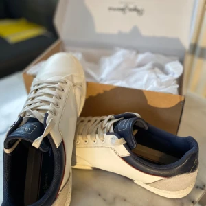 Vita sneakers från Pepe Jeans - Snygga vita sneakers från Pepe Jeans med marinblå detaljer och snörning. Skorna har en stilren design med en bekväm passform och en slitstark sula. Perfekta för en avslappnad stil. Nypris 1300