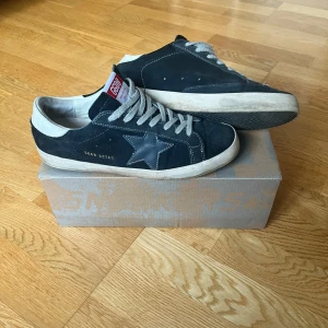  Golden Goose sneakers - Snygga marinblå sneakers från Golden Goose med vit sula och grå snörning. Skorna har en stjärndetalj på sidan och en röd etikett på plösen. Perfekta för en avslappnad stil. Har lite heel drag på en skon men går definitivt att limma. Hör av er med frågor och funderingar. KAN ÄVEN BYTAS, KOM MED FÖRSLAG.