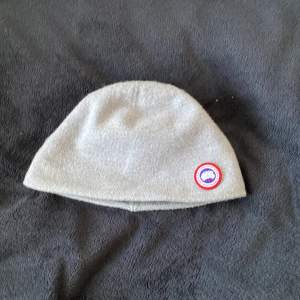 Snygg grå mössa med en broderad logotyp på sidan. Perfekt för kyliga dagar och enkel att matcha med olika outfits. Den är mjuk och bekväm att bära.