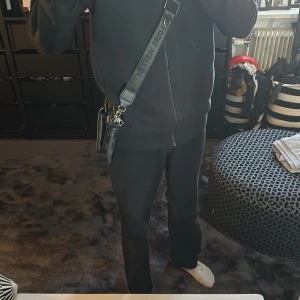 Svart axelväska med monogram - Snygg svart axelväska med monogrammönster och justerbar axelrem. Väskan har flera dragkedjor för säker förvaring och en stilren design som passar perfekt för vardagsbruk.