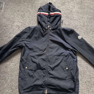 Svart vindjacka från Moncler - Säljer en stilren svart vindjacka från Moncler med huva och dragkedja🤩. Jackan har ett broderat Moncler-märke på ärmen och snörning i huvan🥰. Perfekt för blåsiga dagar🌬️. Tvär fet och svin bra skick!! Såklart äkta,✅ (har order bekräftelse)🧾. 