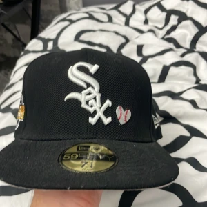 Svart keps från New Era - Snygg svart keps från New Era med broderad logga och text. Kepsen har en World Series-märke på sidan och texten 'Love & Hustle = Game' på baksidan. Tillverkad i polyester och har en klassisk 59FIFTY passform.
