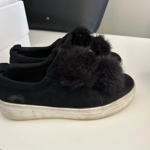 Svarta sneakers med pälsdetalj - Snygga svarta sneakers med fluffiga pälsdetaljer på ovansidan. Skorna har en vit sula som ger en cool kontrast till det svarta. Perfekta för en trendig look.