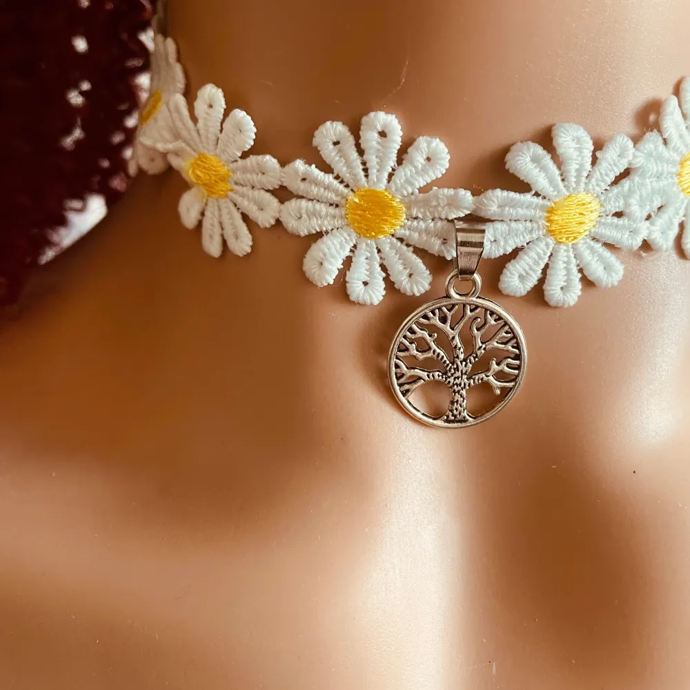 Charmig choker med vita blommor och ett silverfärgat hänge föreställande livets träd. Blommorna har gula mittpunkter som ger en fin kontrast. Perfekt för att ge en bohemisk touch till din stil.. Asusteet.