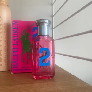 Ralph Lauren parfym för kvinnor - En fräsch och livlig parfym från Ralph Lauren för kvinnor. Flaskan är rosa med en stor blå siffra 2 på framsidan och har en silverfärgad kork. Förpackningen är i en stark rosa färg med grönt tryck av Ralph Lauren-logotypen.