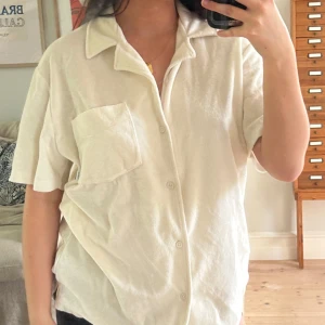 Krämvit kortärmad skjorta från Woodbird - Säljer en krämvit skjorta från Woodbird i storlek S. Skjortan har korta ärmar, klassisk krage, knäppning framtill och en bröstficka. Materialet känns mjukt och lite frottéaktigt, perfekt för en avslappnad stil.