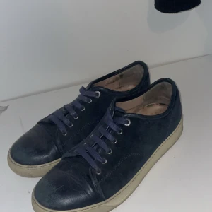 Lanvin mörkblåa - Snygga mörkblå sneakers med klassisk design och vit platt sula. Skorna har rund tå och snörning framtill. Perfekta för en avslappnad och stilren look.