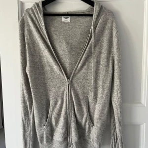 Ljusgrå hoodie med dragkedja från John Henric - Mjuk och stilren ljusgrå cashmere hoodie från John Henric. Tröjan har dragkedja framtill, två fickor och huva med snören. Perfekt för en avslappnad look och passar till det mesta.